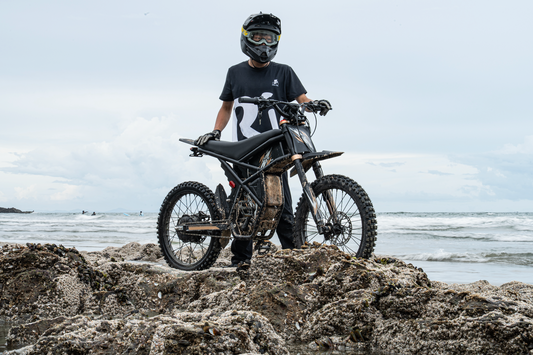 Person wearing helmet standing with black electric bike on rocky beach with ocean background addressing throttle delay issue