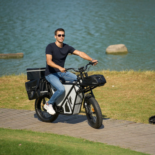 Man riding GT53 electric cargo bike with large cargo baskets near water on wooden path