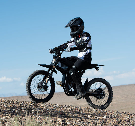 Rider on a black electric dirt bike riding off-road on rocky terrain under clear blue sky top 5 ebikes of 2025