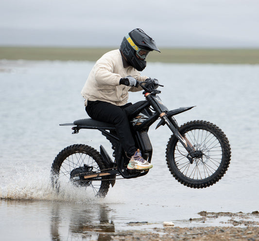 Rider performing a wheelie on a Riding Times e-Bike off-road through shallow water.