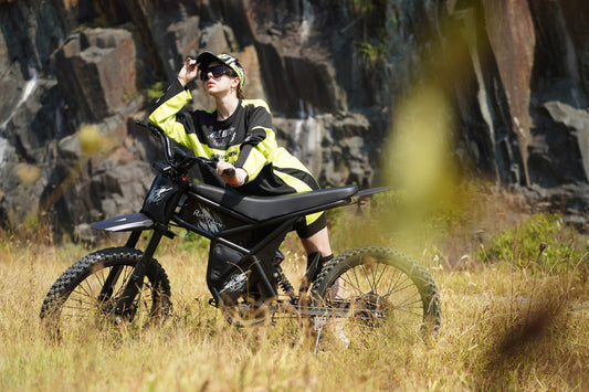 Rider posing on the black Riding Times GT73 Pro electric off-road bike in grassy outdoor setting with rocky background