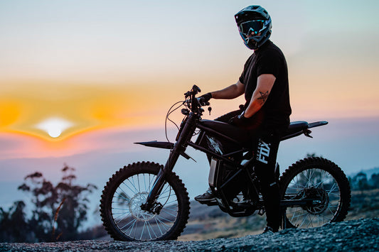 Rider wearing helmet on Riding Times e-bike electric dirt bike at sunset for safety awareness in 2025