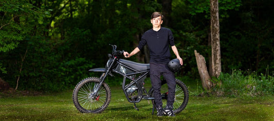 Teen standing beside GT73 electric motorbike holding a black helmet in a green outdoor setting