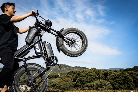 A young man propping up his ebike on the rear wheel, with the hills and the blue sky as a background