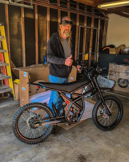 Man giving thumbs up beside a black electric bike in a garage setting