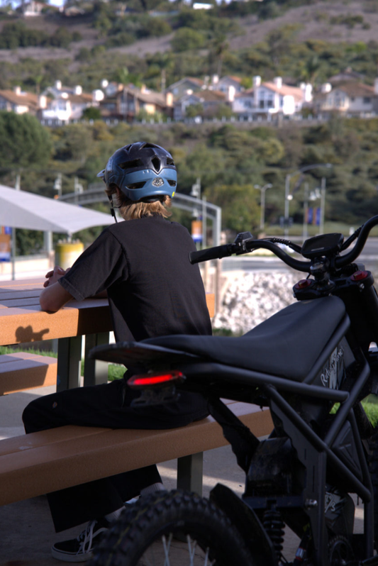 Person wearing helmet sitting on bench next to black GT73 Pro eBike with scenic hillside houses in background