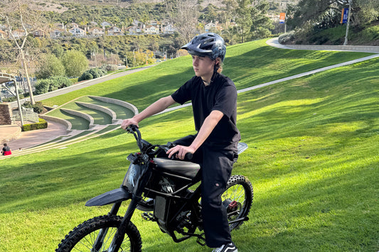 Child wearing helmet riding a black Riding Times Z8 electric bike on grassy hill in park