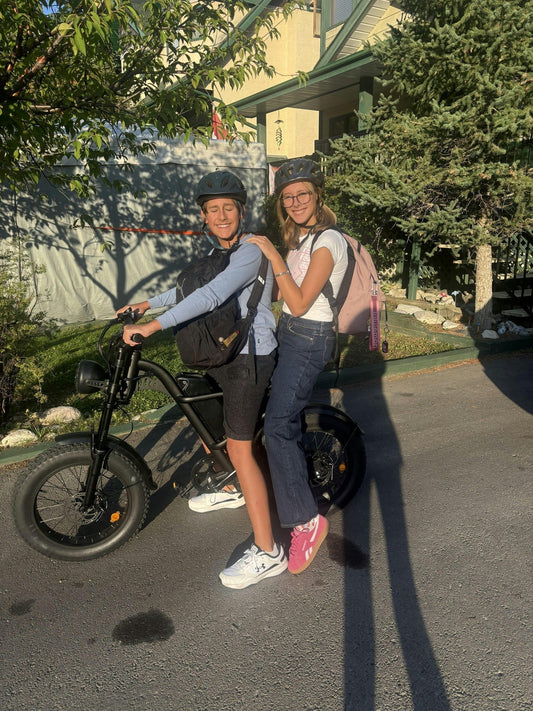 Two people wearing helmets riding a street-legal Class 3 electric bike on a residential street, representing the E-Bike Classification Guide
