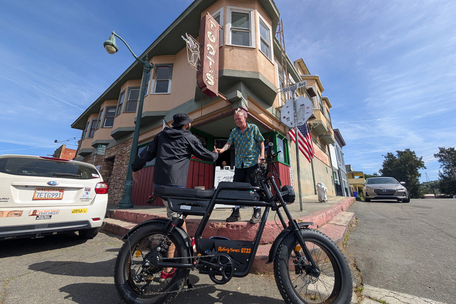Low-angle street view of the Riding Times GT33 cargo electric bike parked at an urban corner as a rider receives a delivery, demonstrating real-world cargo and commuter use