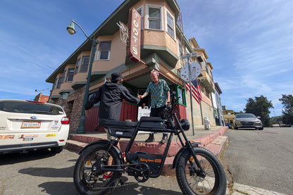 Low-angle street view of the Riding Times GT33 cargo electric bike parked at an urban corner as a rider receives a delivery, demonstrating real-world cargo and commuter use