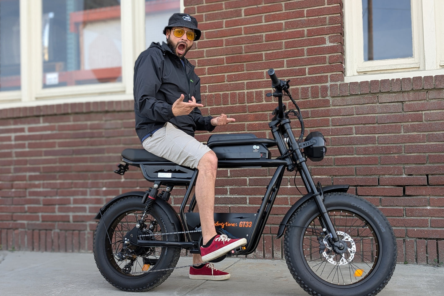 Excited rider on the Riding Times GT33 cargo eBike in front of a brick building, showcasing the moped-style cafe racer design in an urban setting