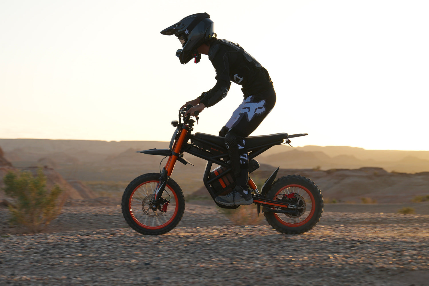 Person riding GT54 electric mini motorbike for kids and adults on rocky terrain at sunset