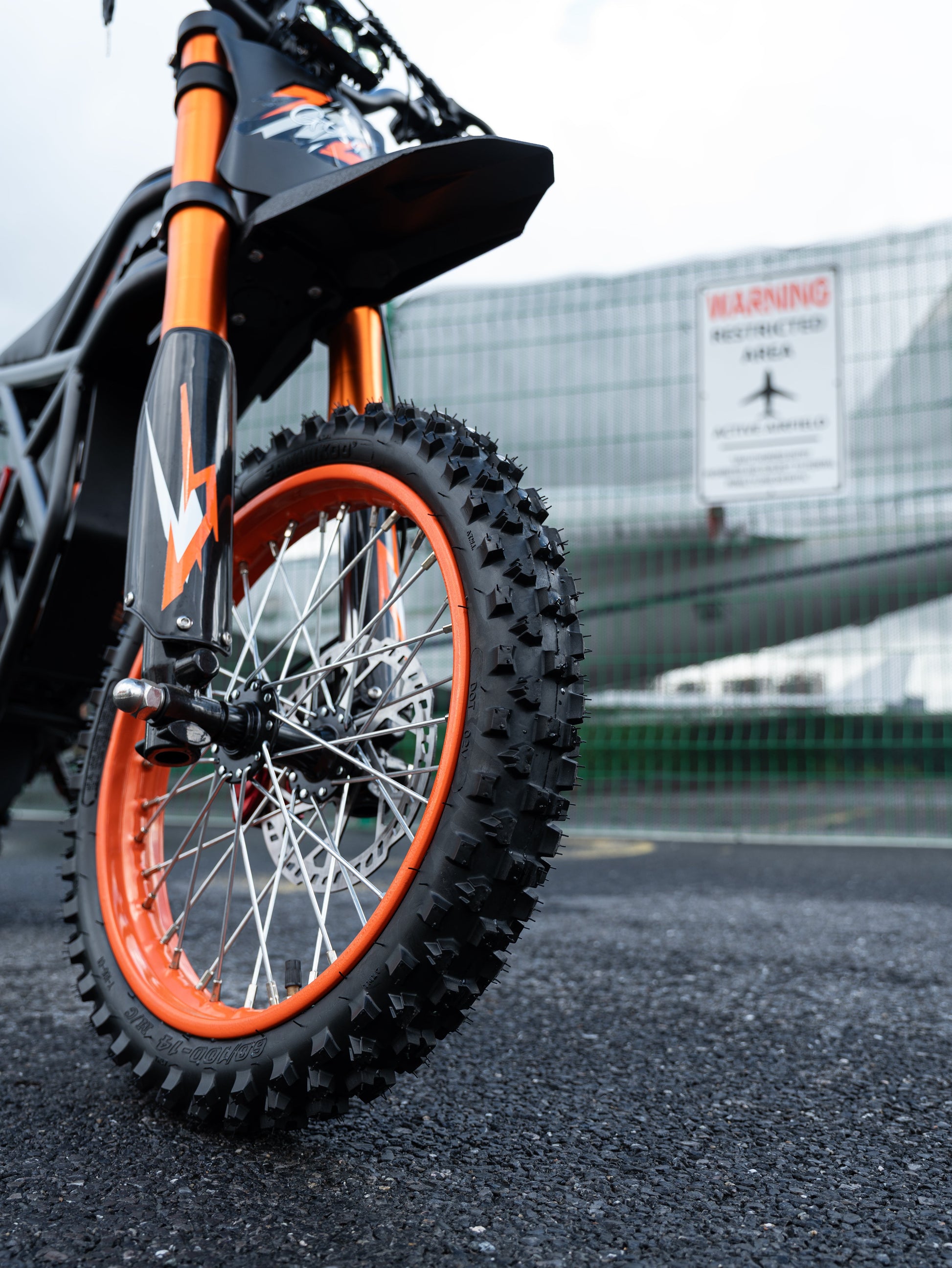 GT54 electric mini motorbike front tire with orange rim on asphalt near airport fence