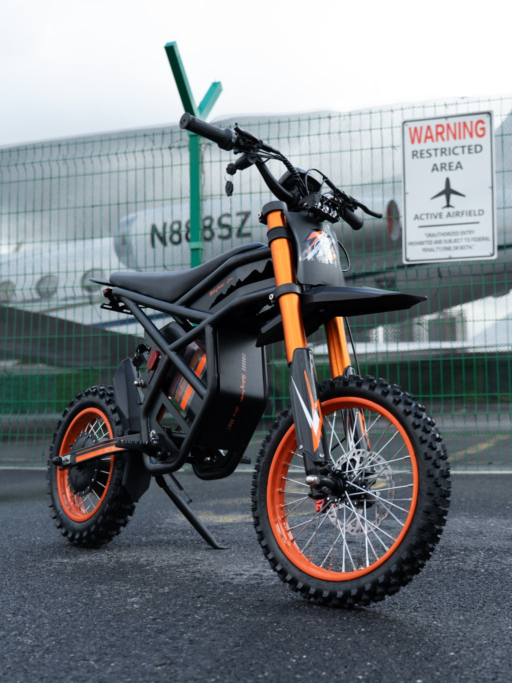 GT54 electric mini motorbike with orange accents and off-road tires parked near airfield fence