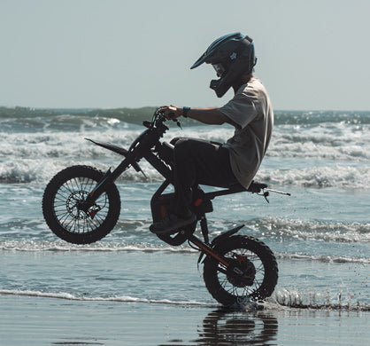 Person riding a small motorcycle on a beach with waves in the background