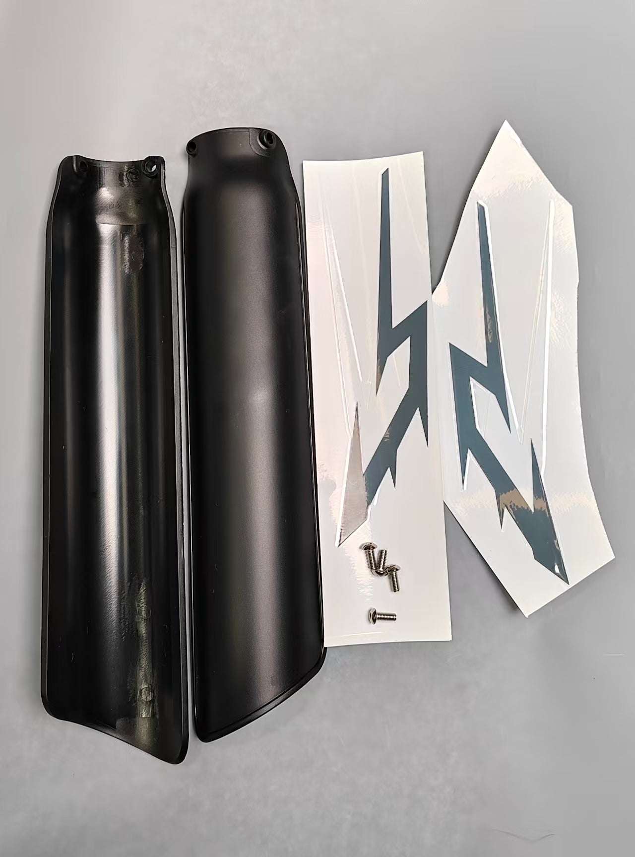 Black front fork guard covers with white graphic decals and mounting screws on gray surface